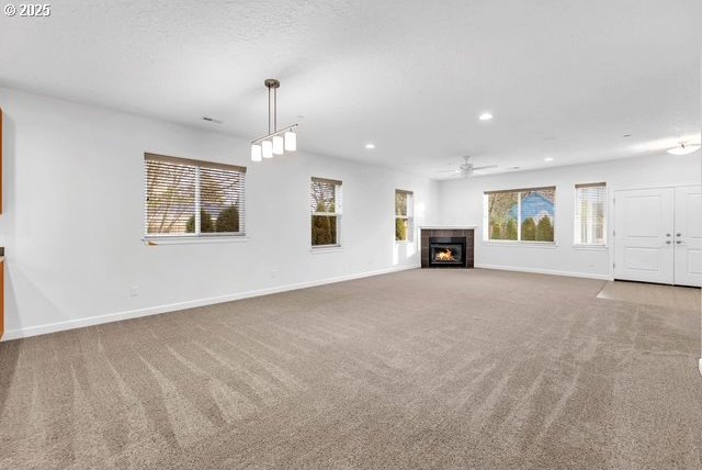 unfurnished living room with a healthy amount of sunlight, a tiled fireplace, and light carpet