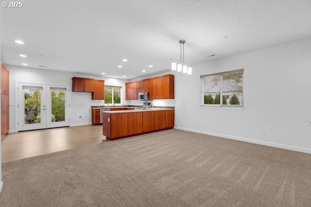 kitchen with pendant lighting, appliances with stainless steel finishes, kitchen peninsula, light carpet, and french doors