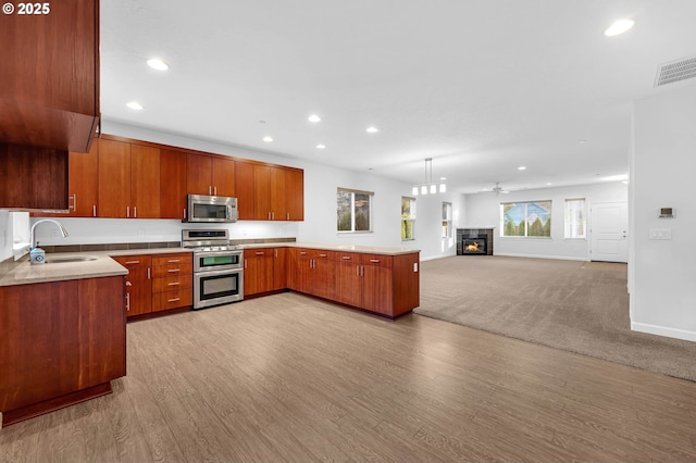 kitchen featuring sink, hanging light fixtures, kitchen peninsula, stainless steel appliances, and light hardwood / wood-style floors