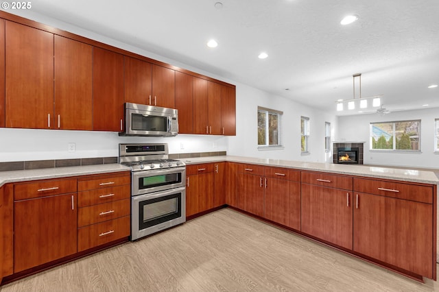 kitchen featuring light hardwood / wood-style flooring, hanging light fixtures, stainless steel appliances, a fireplace, and a textured ceiling