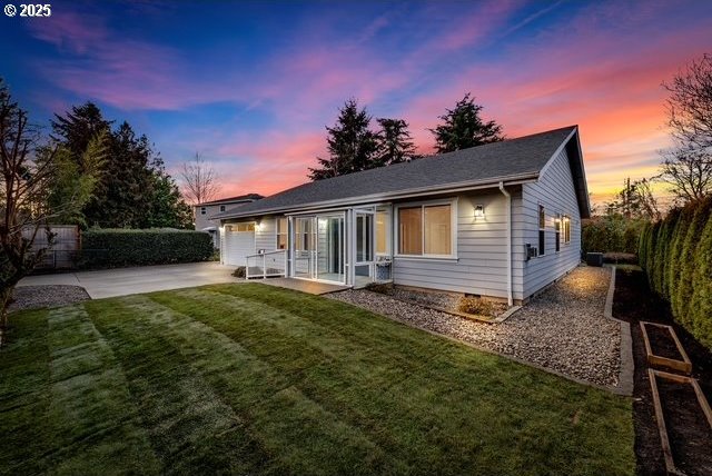 back house at dusk featuring a patio and a lawn