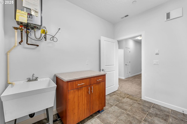 laundry area with water heater, sink, and a textured ceiling