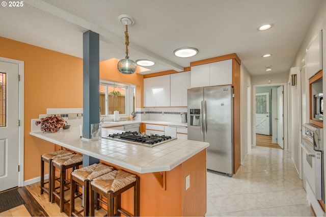 18989 NE Marine Dr Unit 04, Portland, OR 97230 - kitchen featuring appliances with stainless steel finishes, tile counters, white cabinetry, a kitchen bar, and a peninsula