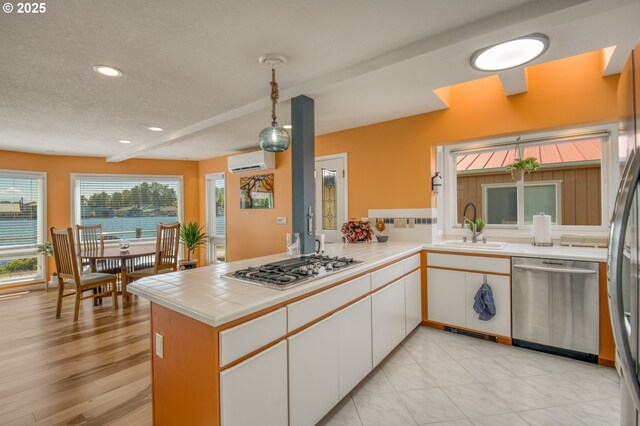 18989 NE Marine Dr Unit 04, Portland, OR 97230 - kitchen featuring appliances with stainless steel finishes, a wall mounted air conditioner, white cabinets, a peninsula, and a textured ceiling