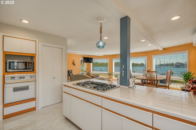 18989 NE Marine Dr Unit 04, Portland, OR 97230 - kitchen with stainless steel appliances, white cabinets, recessed lighting, decorative light fixtures, and tile countertops