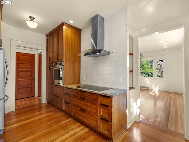 1925 Irving Ave, Astoria, OR 97103 - kitchen with wall chimney exhaust hood, appliances with stainless steel finishes, light wood finished floors, brown cabinetry, and light stone counters