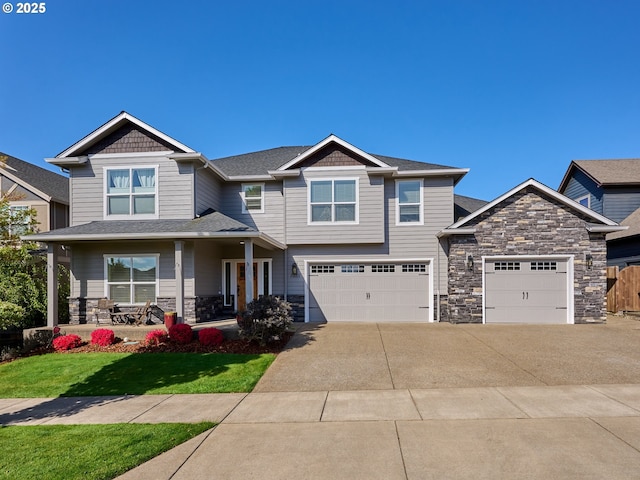 craftsman-style home with a garage, a front lawn, covered porch, stone siding, and driveway