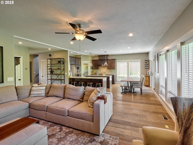 living area with visible vents, recessed lighting, a textured ceiling, a ceiling fan, and light wood-style flooring
