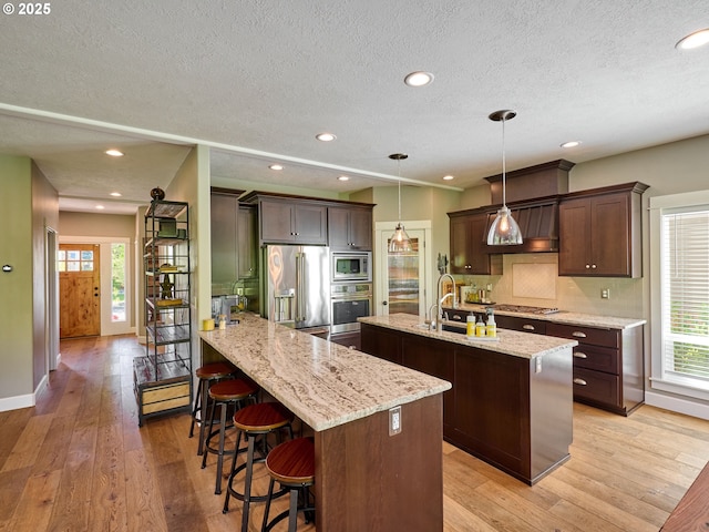 kitchen with appliances with stainless steel finishes, plenty of natural light, a textured ceiling, and an island with sink