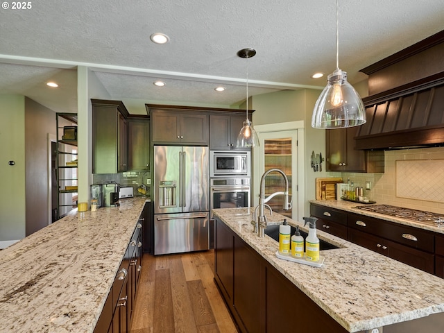 kitchen with dark brown cabinetry, a textured ceiling, tasteful backsplash, light wood finished floors, and appliances with stainless steel finishes