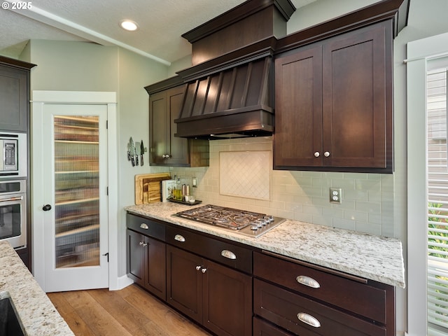 kitchen featuring backsplash, stainless steel appliances, dark brown cabinets, and light wood-type flooring