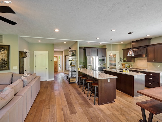 kitchen with stainless steel appliances, open floor plan, an island with sink, and a textured ceiling