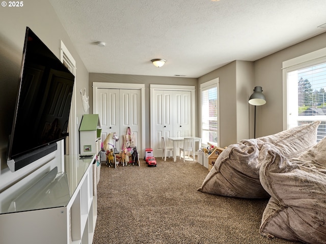 carpeted bedroom with a textured ceiling, two closets, and multiple windows