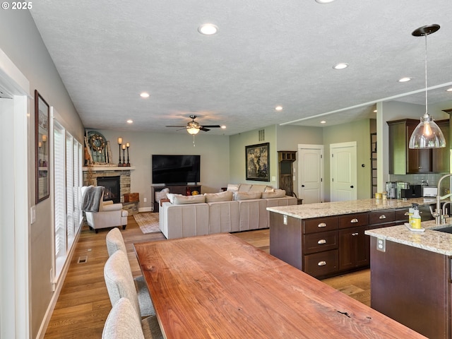 dining area featuring a stone fireplace, baseboards, recessed lighting, a ceiling fan, and light wood-style flooring