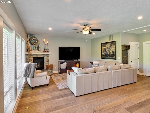 living area featuring ceiling fan, visible vents, a stone fireplace, and light wood finished floors