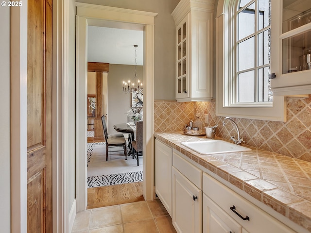 kitchen with sink, white cabinets, tile counters, a notable chandelier, and light tile patterned floors