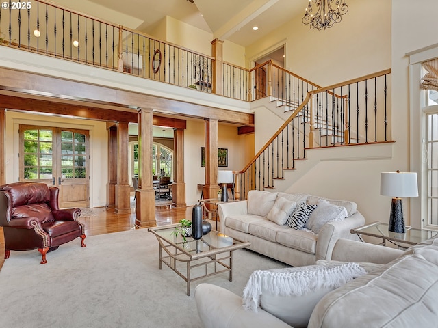 carpeted living room featuring french doors, a towering ceiling, an inviting chandelier, and ornate columns