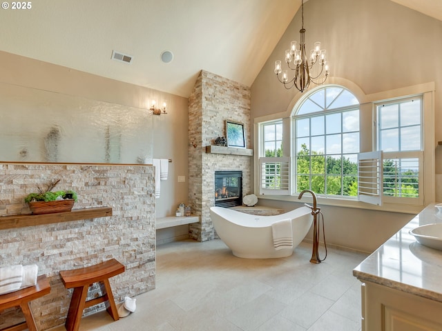 bathroom with a stone fireplace, an inviting chandelier, high vaulted ceiling, vanity, and a bathing tub