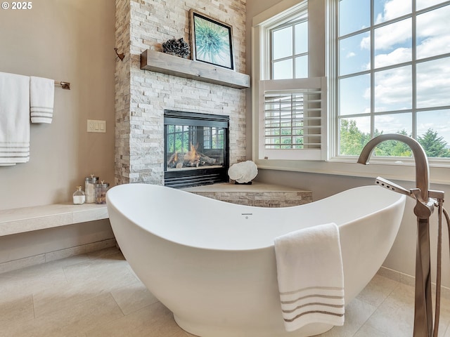 bathroom with tile patterned floors, a tub to relax in, a stone fireplace, and a wealth of natural light