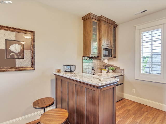 bar with light hardwood / wood-style flooring, black microwave, dishwasher, light stone countertops, and backsplash