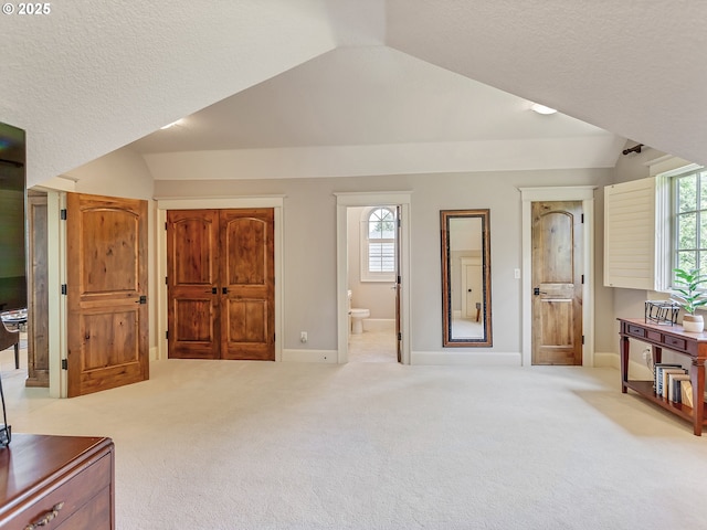 bedroom with lofted ceiling, light colored carpet, and ensuite bathroom