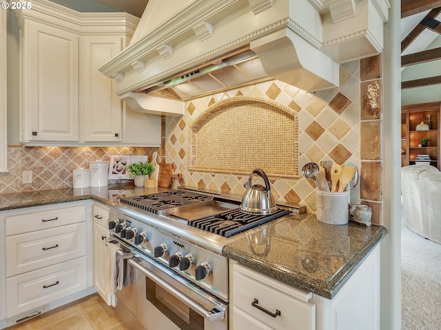 kitchen featuring premium range hood, white cabinets, backsplash, dark stone counters, and range with two ovens