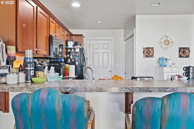 kitchen with black appliances, a kitchen breakfast bar, brown cabinetry, and a textured ceiling