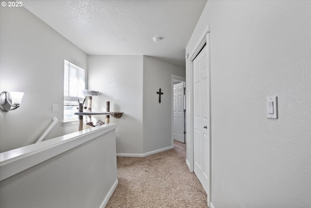 hall featuring light colored carpet, a textured ceiling, and baseboards