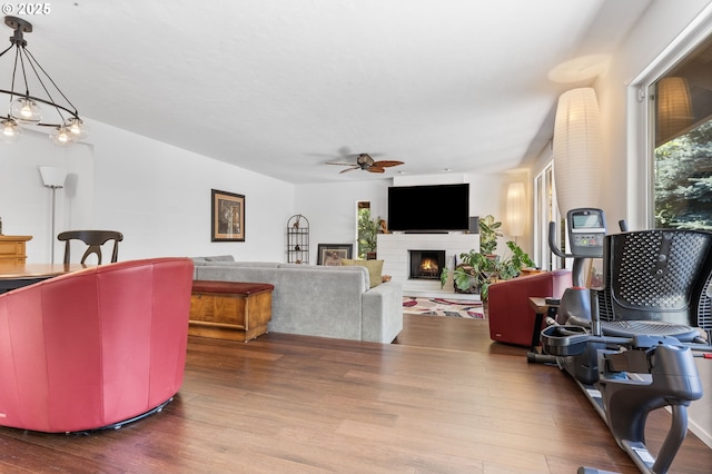 living room with ceiling fan with notable chandelier, hardwood / wood-style floors, and a brick fireplace