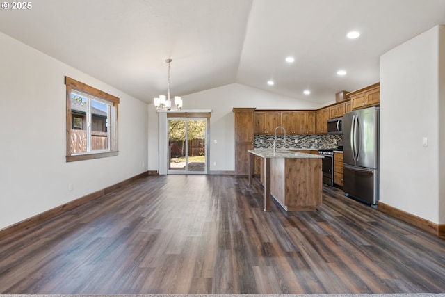 kitchen featuring appliances with stainless steel finishes, a chandelier, vaulted ceiling, dark wood finished floors, and a center island with sink