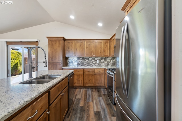 kitchen featuring stainless steel appliances, a sink, lofted ceiling, dark wood-style flooring, and brown cabinetry
