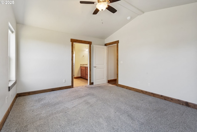 unfurnished bedroom featuring baseboards, vaulted ceiling, light colored carpet, ensuite bath, and a ceiling fan
