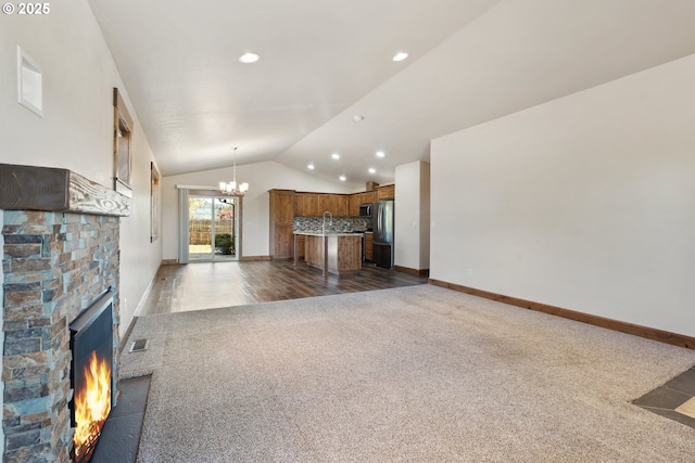 unfurnished living room with dark colored carpet, lofted ceiling, a chandelier, a fireplace, and baseboards