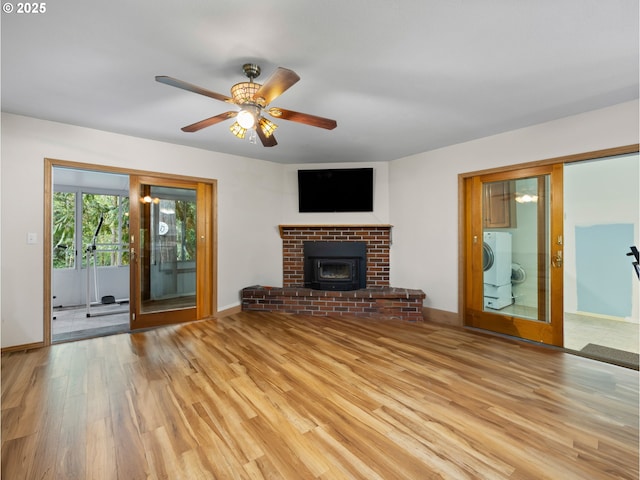 unfurnished living room with a brick fireplace, washer / dryer, light hardwood / wood-style floors, and ceiling fan