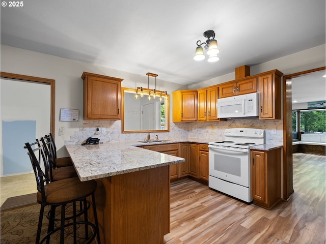 kitchen with pendant lighting, sink, white appliances, a breakfast bar area, and kitchen peninsula