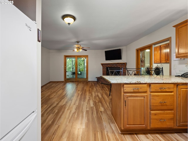 kitchen featuring a fireplace, white fridge, ceiling fan, light stone counters, and light hardwood / wood-style floors