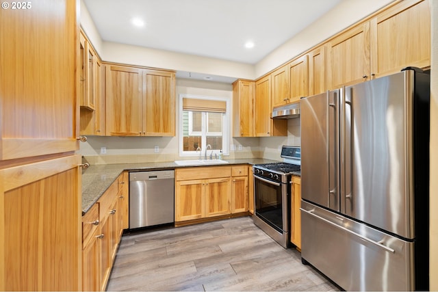 kitchen featuring appliances with stainless steel finishes, light wood-type flooring, light brown cabinetry, dark stone countertops, and sink