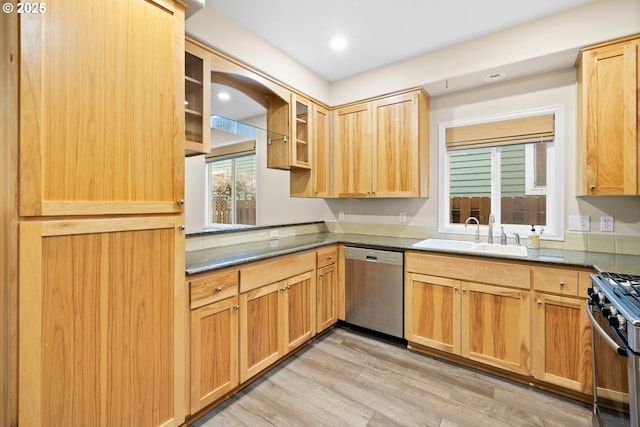 kitchen with appliances with stainless steel finishes, light hardwood / wood-style floors, dark stone counters, and sink