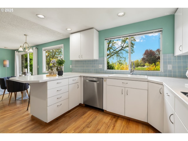 kitchen with a sink, a peninsula, light wood-style flooring, and dishwasher