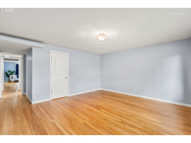 spare room with baseboards, light wood-type flooring, and a textured ceiling