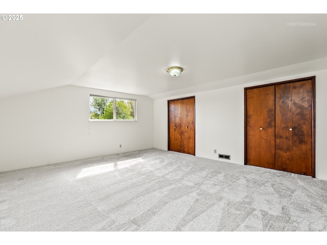 unfurnished bedroom featuring multiple closets, lofted ceiling, carpet floors, and visible vents