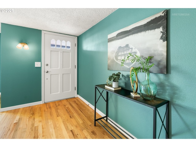foyer entrance with a textured ceiling, baseboards, and wood finished floors