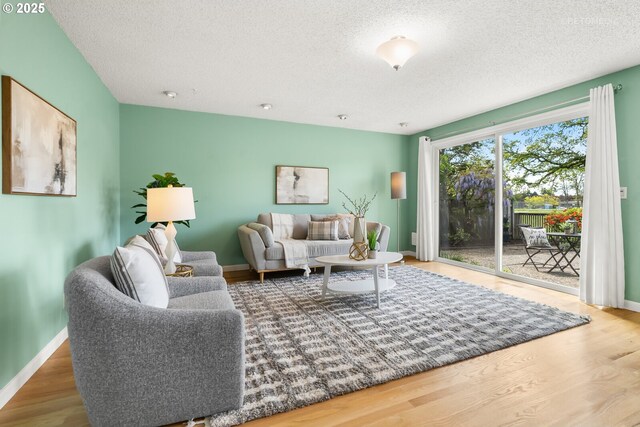 living room with a textured ceiling, baseboards, and wood finished floors