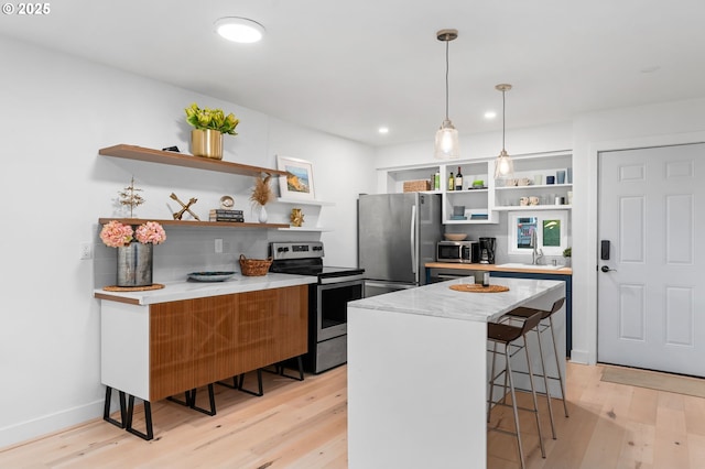 kitchen featuring light wood-style floors, open shelves, stainless steel appliances, and a breakfast bar area