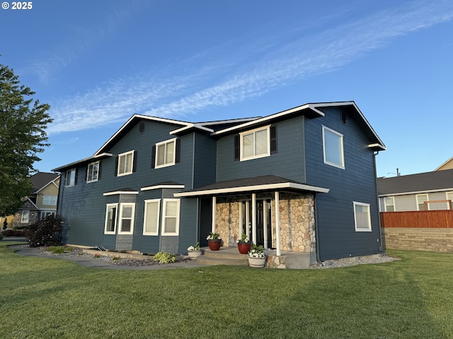 view of front of home with covered porch, stone siding, a front lawn, and fence