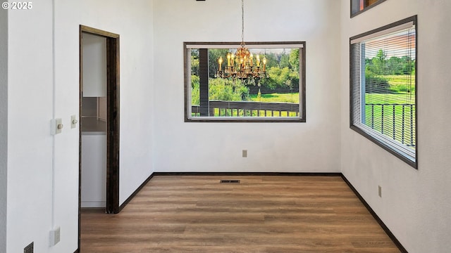 unfurnished dining area featuring visible vents, baseboards, an inviting chandelier, and wood finished floors