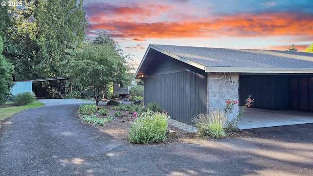 property exterior at dusk featuring stone siding, a shingled roof, and an outdoor structure