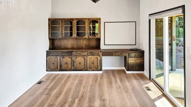 interior space with light wood-type flooring, visible vents, baseboards, and built in desk