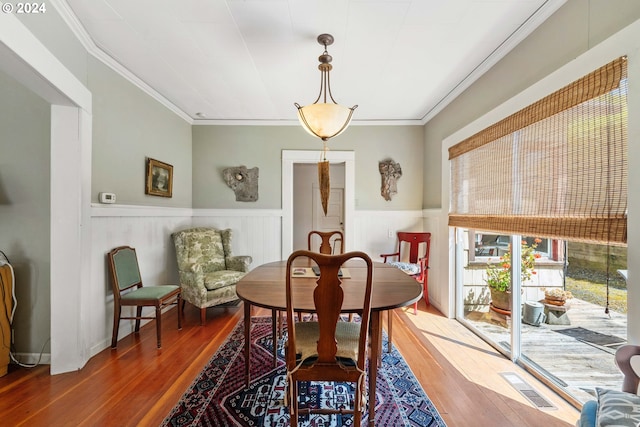 dining area with wainscoting, ornamental molding, wood finished floors, and visible vents