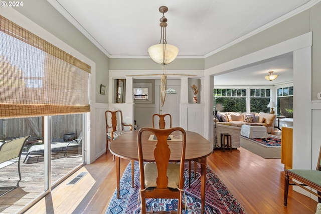 dining space with ornamental molding, a wainscoted wall, light wood-style floors, visible vents, and a decorative wall